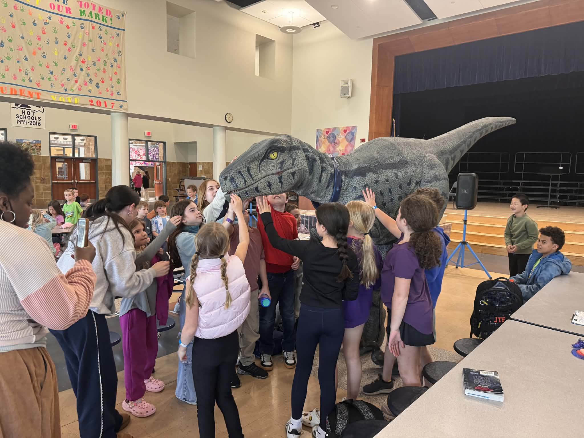 Primal the Raptor dinosaur character interacting with excited children at school assembly in Connecticut