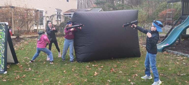 Group of 8 year old kids playing laser tag in backyard with blasters and vests during birthday party