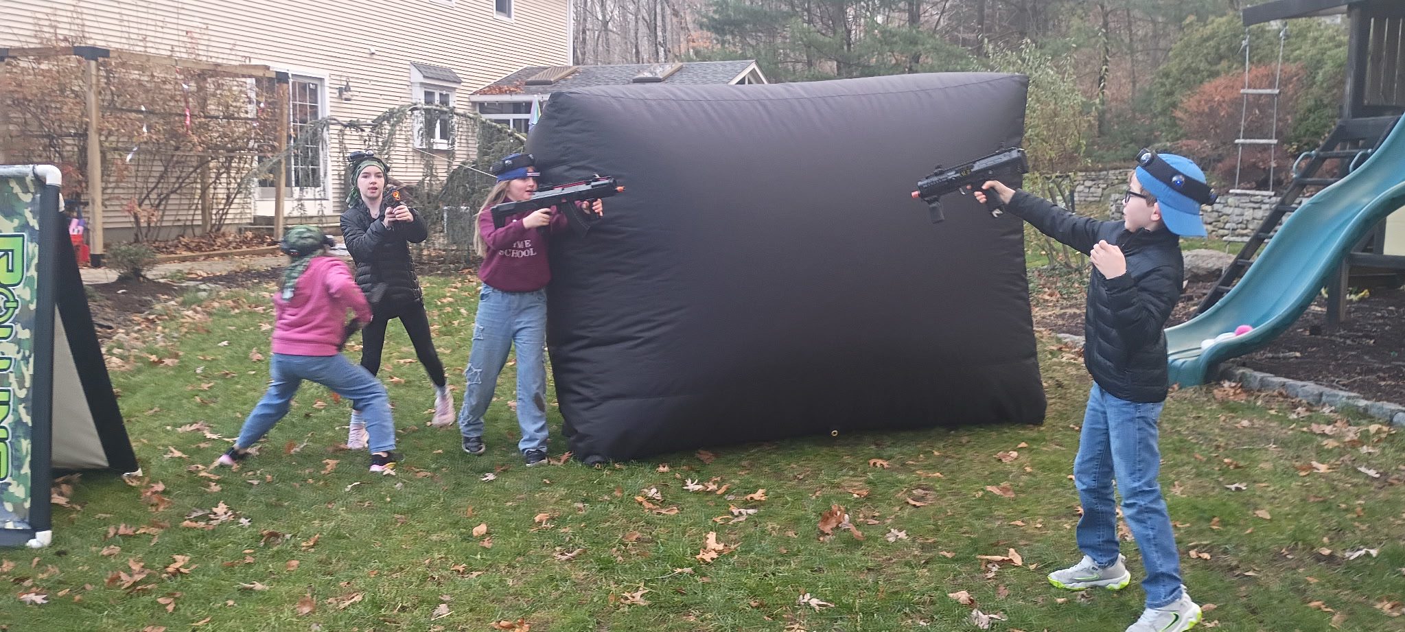 Group of 8 year old kids playing laser tag in backyard with blasters and vests during birthday party