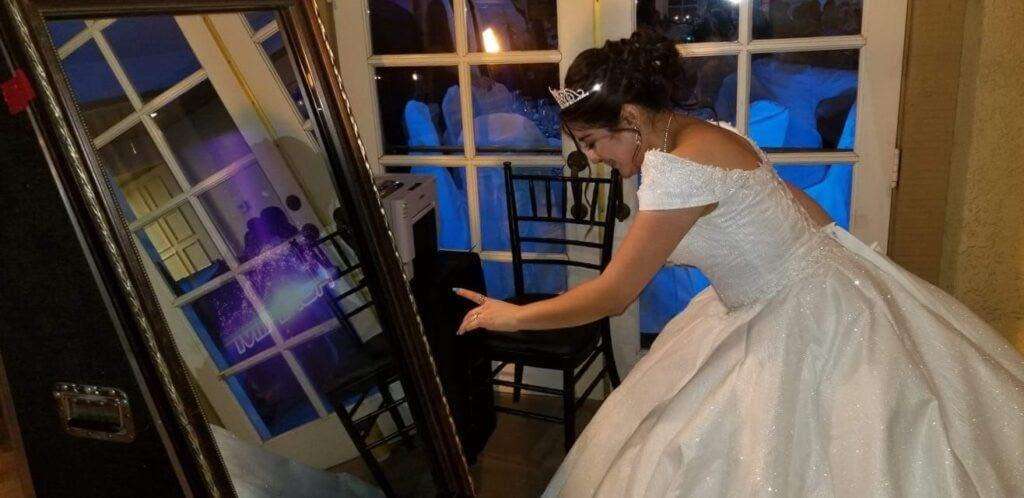 Teen girl touching the interactive mirror photo booth at a quinceañera or Sweet 16 celebration.